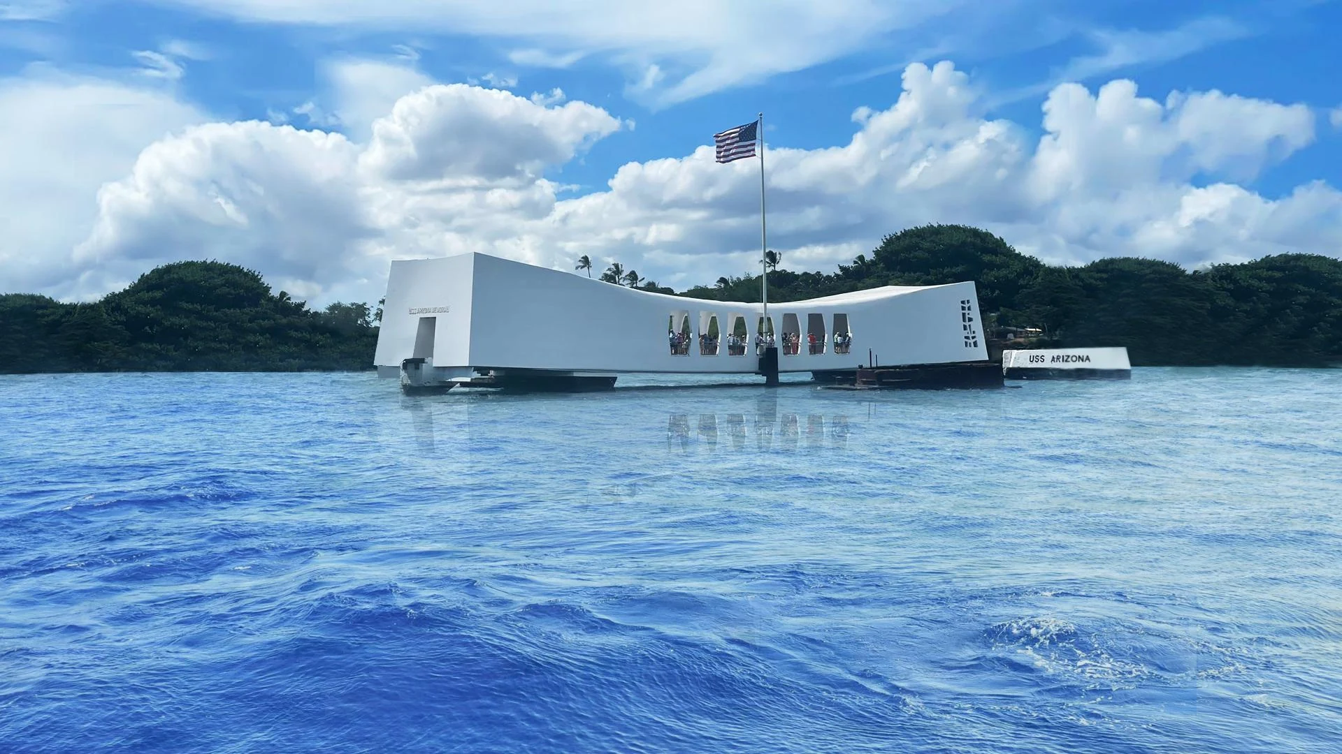 USS Arizona Memorial above the waters of Pearl Harbor beneath a bright blue sky